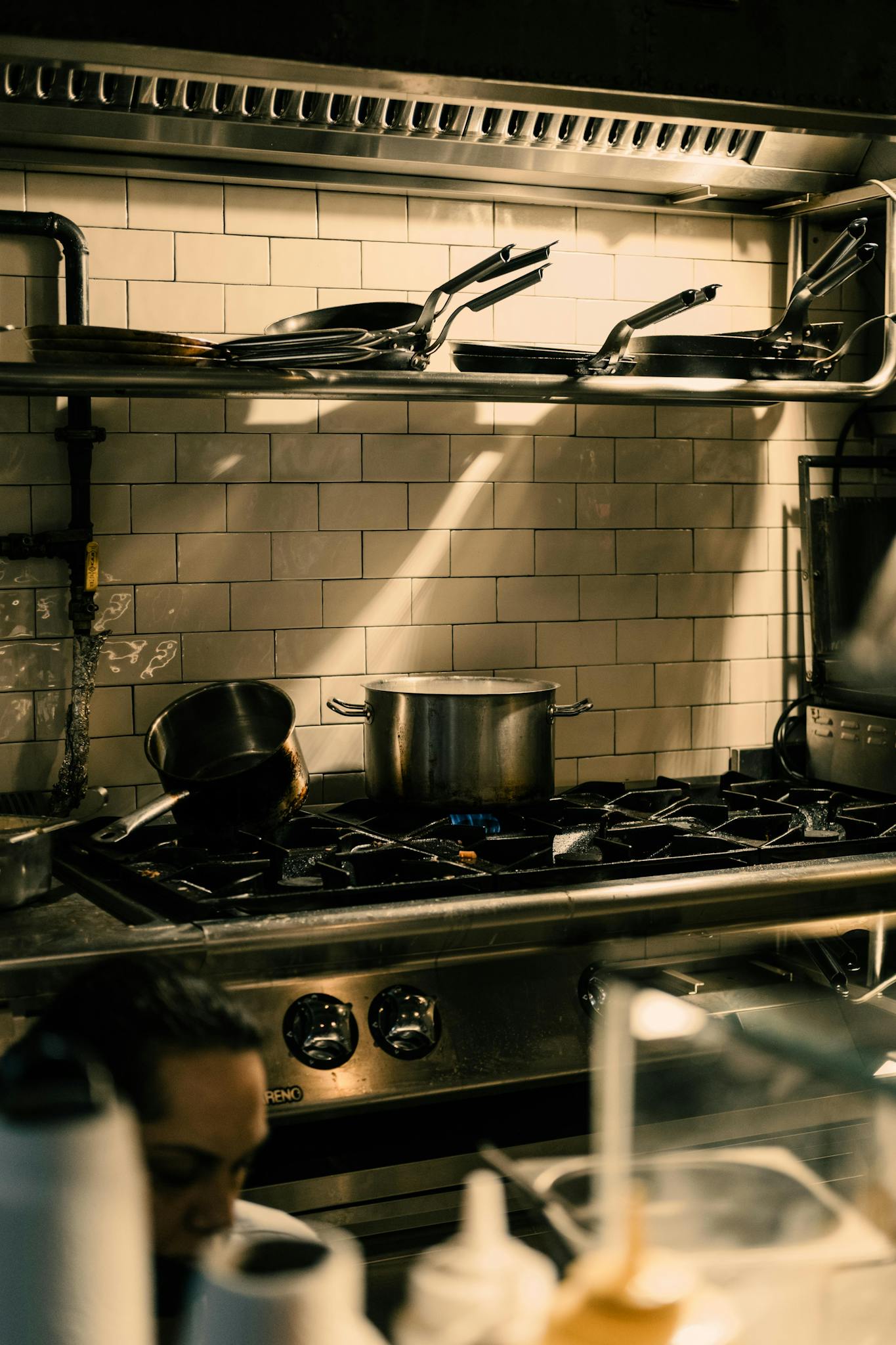 A well-equipped restaurant kitchen with pans and pots on a stove under warm lighting.